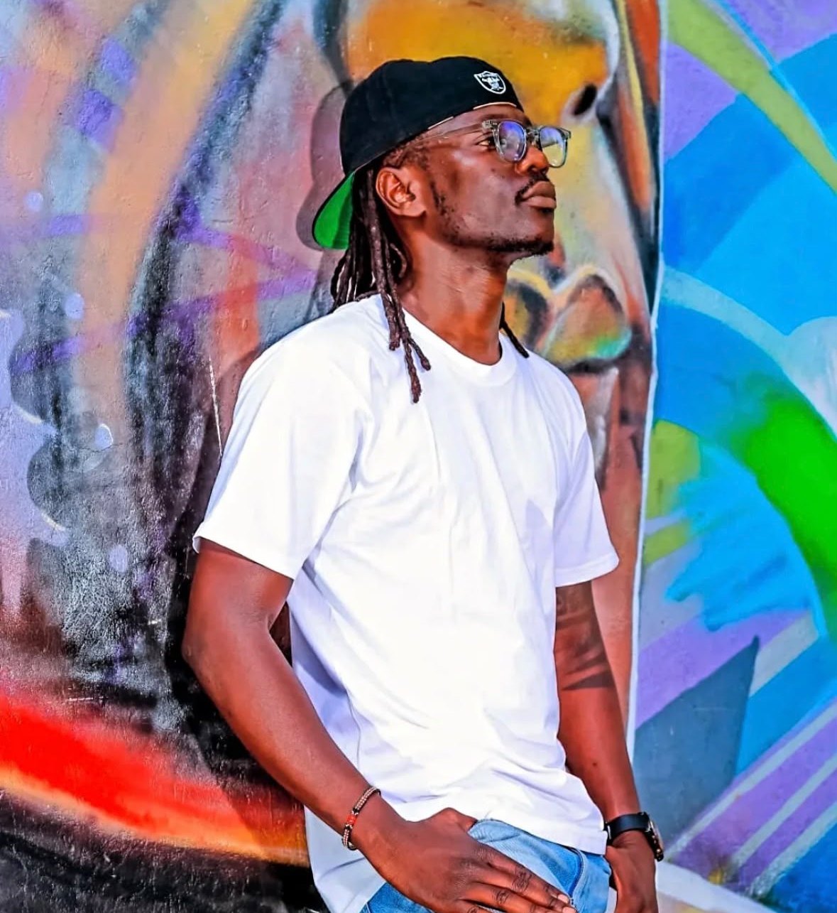 DJ BMT leaning against a graffiti wall
